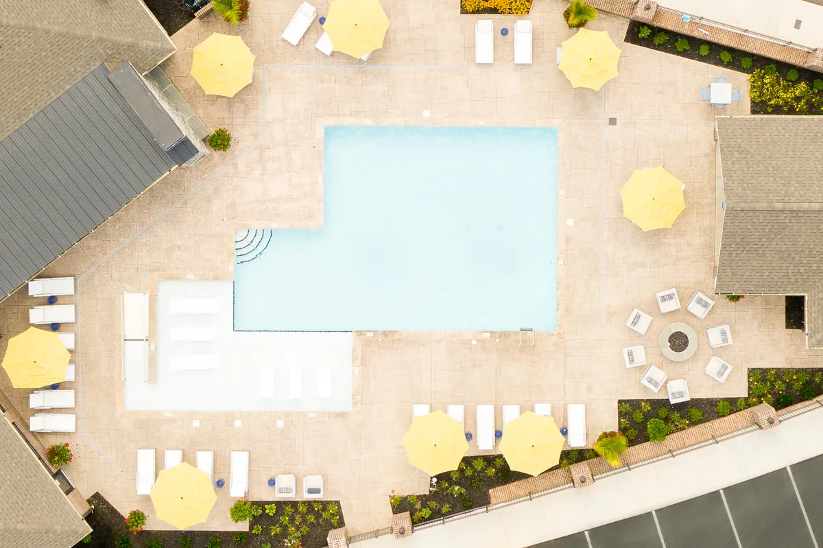 A vibrant pool area with yellow umbrellas, lounge chairs, and a cozy fire pit, all set in a cheerful atmosphere. The poolside environment suggests both relaxation and the potential for solo or social enjoyment, perfectly capturing the leisure options available to residents.