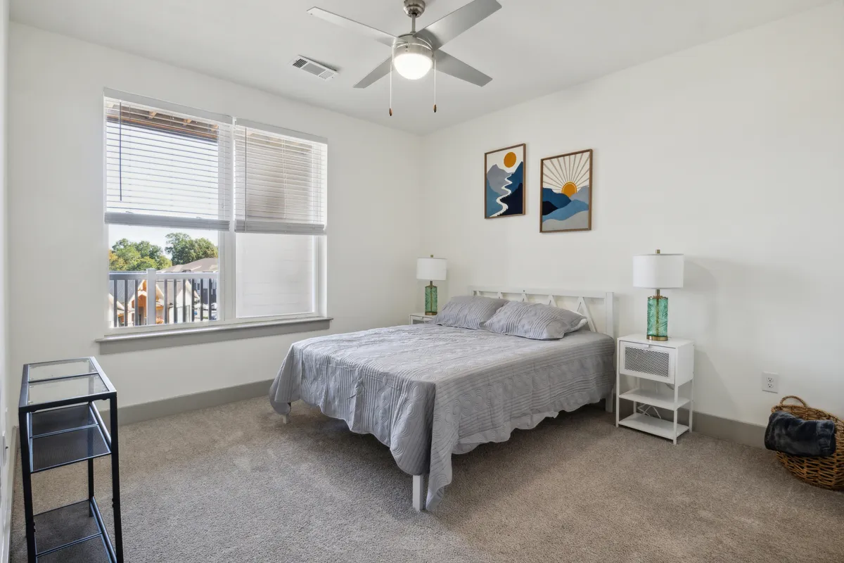 A tranquil bedroom scene featuring a plush bed with luxury linens, soft bedside lamps, tasteful wall art, and a window with coverings that allow for restful sleep or gentle natural light. The inviting setup communicates comfort and privacy.