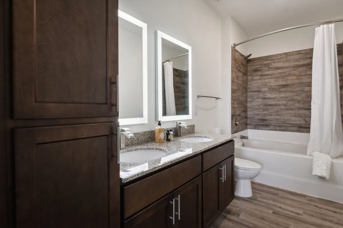 A modern bathroom featuring a double sink vanity, large mirrors, a stylish bathtub, and wood-textured wall accents. Fresh towels and complimentary toiletries enhance the spa-inspired feel, perfect for morning routines or relaxing baths.