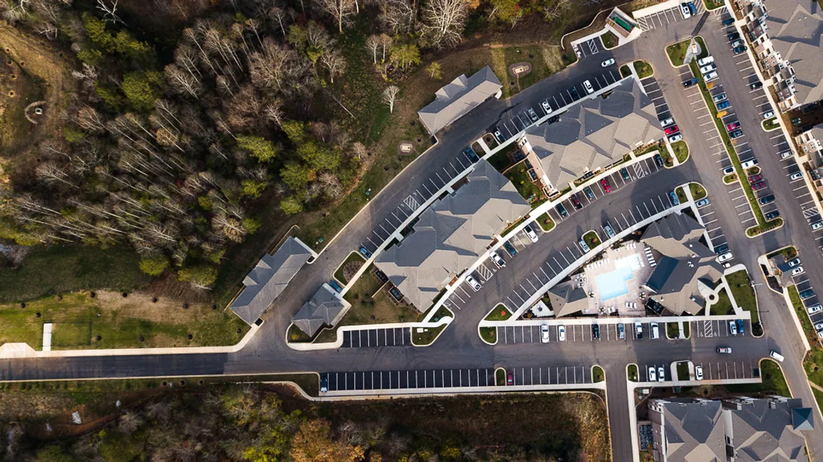 A wider exterior view showcasing apartment buildings, a parking lot for easy commuting, landscaped areas, and a swimming pool. The space looks inviting and community-oriented, with amenities that encourage both productivity and relaxation close to home.