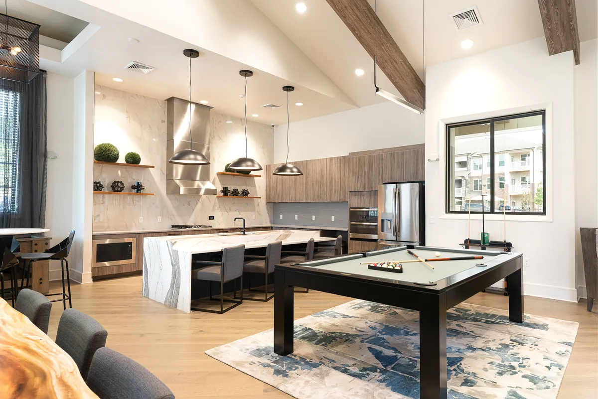 A lively common area with a pool table, kitchen island, and seating for gatherings. Exposed wooden beams and a dining area create a sociable, welcoming atmosphere.