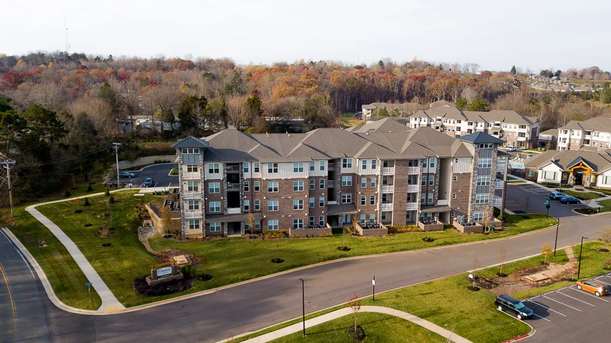 An exterior view of the multi-story building surrounded by landscaped lawns, mature trees, and a spacious parking area. The environment feels open, inviting, and slightly secluded—suggesting a tranquil retreat just moments from the city’s lively districts.