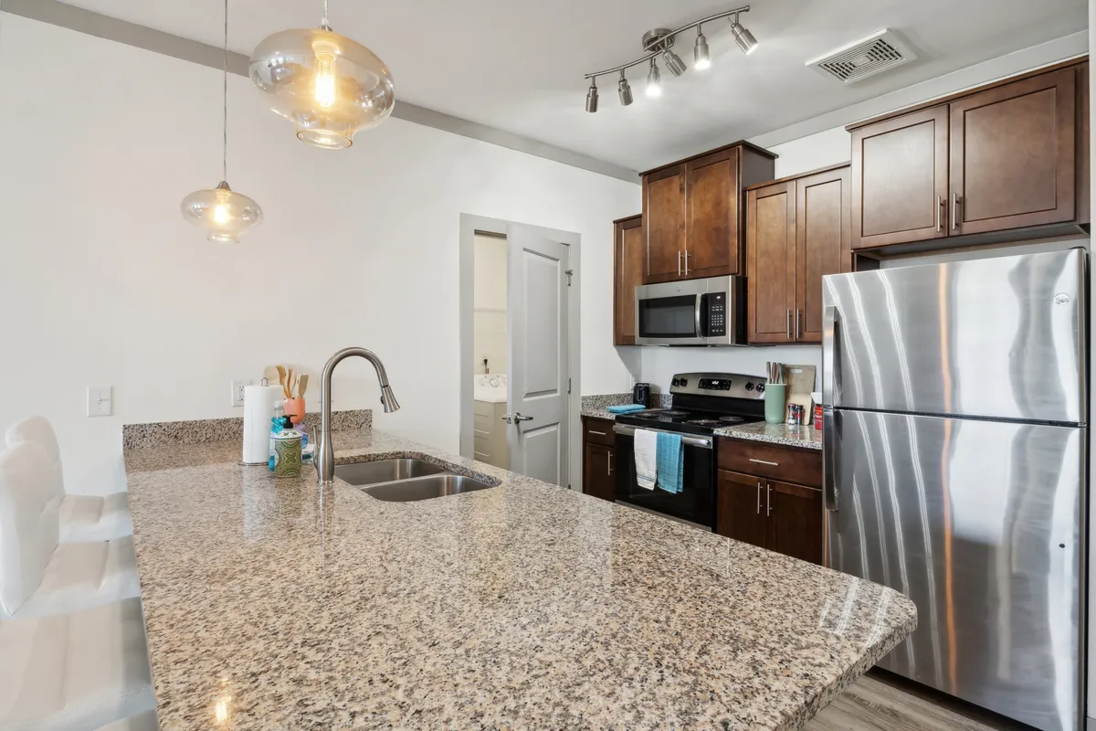 A welcoming kitchen setting with a prominent granite countertop, stainless steel appliances, modern light fixtures, and warm wooden cabinets. The space is styled to evoke a sense of gathering, suggesting both everyday meal prep and festive entertaining.
